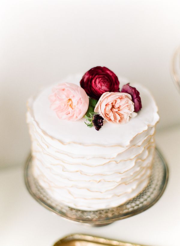 Image of a white wedding cake with three peach and cranberry flowers.
